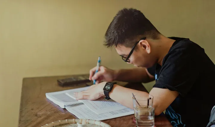 책상에서 노트에 글을 쓰는 학생